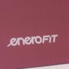 Na zdjęciu widoczna jest mata do jogi w kolorze bordowym z białym logo "eneroFIT" na powierzchni o wzorze w jodełkę.