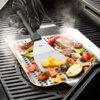 Na zdjęciu widoczna jest szpatułka z napisem "GEFU" używana do przewracania grillowanych warzyw na metalowej tacy z otworami, z której unosi się para. Warzywa to m.in. papryka, cukinia, pieczarki i pomidorki koktajlowe.