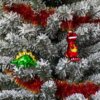Na zdjęciu widoczna jest choinka ozdobiona czerwono-złotym łańcuchem oraz dwiema bombkami w kształcie dinozaurów: zielonym i czerwonym. Gałęzie choinki pokryte są sztucznym śniegiem.