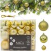 Na zdjęciu znajduje się zestaw złotych bombek choinkowych w plastikowym opakowaniu, z widocznym napisem: "MICA Decorations, Christmas baubles, recycled plastic, 46 pcs". W tle widać gałązki choinki ozdobione bombkami.