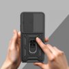 Czarne etui TECH-PROTECT Camshield Pro do Xiaomi Redmi 15 4G/5G jest trzymane w dłoniach, z widocznym przesuwanym elementem ochronnym na aparat oraz uchwytem na palec. Tło jest szare, a etui ma teksturowaną powierzchnię z geometrycznymi wzorami.