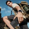 Mężczyzna w jasnej koszulce i ciemnych szortach wspina się po skałach, trzymając w ręku czarne etui TECH-PROTECT Camshield Pro. Na nadgarstku ma założony smartwatch, a na plecach duży plecak z przypiętym zielonym pojemnikiem.