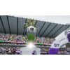 Na zdjęciu znajduje się srebrny puchar z koroną na szczycie, z napisem "Premier League" na froncie. W tle widać trybuny stadionu z kibicami oraz fragmenty banerów i łuk z napisem "CHAMPIONS".