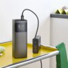 Szary powerbank HAMA High Power 24000 mAh 150W stoi na żółtej powierzchni, z podłączonym kablem, a na jego wyświetlaczu widoczne są różne poziomy naładowania i napięcia. Obok znajduje się czarny adapter z kilkoma portami USB, a na nim widoczne są oznaczen