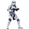 Na zdjęciu znajduje się figurka przedstawiająca szturmowca z serii Star Wars, ubrana w biały pancerz z czarnymi elementami, trzymająca czarną broń. Produkt to "Figurka HASBRO Star Wars The Vintage Collection Szturmowiec G09255X2".