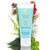 Na zdjęciu znajduje się tubka z napisem "LUMINEO PROFESSIONAL LINE SUPREME CLEANSER FOR ALL SKIN TYPES IDEAL FOR USE WITH FACIAL CLEANSING BRUSHES", otoczona różnorodnymi roślinami, w tym czerwonymi jagodami, fioletowymi kwiatami i zielonymi liśćmi.