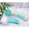 Na zdjęciu znajduje się turkusowa szczoteczka do twarzy z białymi elementami oraz tubka żelu do twarzy z napisem "LUMINEO SUPRIME CLEANER FOR ALL SKIN TYPES". W tle widoczny jest biały ręcznik i zielone liście rośliny.