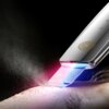 Na zdjęciu widoczne jest urządzenie do peelingu kawitacyjnego z metaliczną obudową i ozdobnym wzorem, emitujące niebieskie i różowe światło na skórę. Wokół urządzenia unosi się delikatna mgiełka.