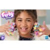 Na zdjęciu widoczny jest zestaw kolorowych figurek z serii "Furby minis" umieszczonych na palcach dziecka, z logo "Hasbro" w prawym dolnym rogu. W lewym górnym rogu znajduje się napis "Furby minis", a w lewym dolnym rogu widnieje oznaczenie wiekowe "5+".