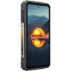 Smartfon z dużym ekranem, na którym wyświetlany jest obraz przedstawiający oświetlony namiot na tle gór i jeziora. Obudowa urządzenia jest solidna, z widocznymi elementami metalowymi i pomarańczowym przyciskiem.