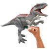 Na zdjęciu znajduje się szara figurka dinozaura z czerwonymi akcentami na grzbiecie, z otwartą paszczą i widocznymi zębami. Dłoń trzymająca figurkę naciska na zielony element pod brzuchem dinozaura.