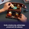 Na zdjęciu widoczny jest zestaw klocków LEGO przedstawiający wnętrze z meblami i akcesoriami, które są manipulowane przez ręce. Na dole zdjęcia znajduje się tekst: "Kufer otwiera się, odsłaniając przestrzeń do zabawy".