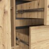 Zbliżenie na wnętrze komody w kolorze Dąb Artisan, ukazujące drewniane szuflady z metalowymi prowadnicami. Widoczne są również fragmenty półek i struktura drewna z naturalnymi sękami.