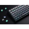 Na zdjęciu znajduje się klawiatura mechaniczna z podświetleniem RGB, z widocznymi klawiszami oznaczonymi literami i symbolami, takimi jak "ESC", "TAB", "CAPS", "SHIFT", "CTRL", "WIN", "ALT". Obok klawiatury leżą kilka zielonych przełączników mechanicznych