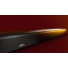 Czarny soundbar z widocznym logo "BOSE" na przedniej kratce, oświetlony żółtym światłem na tle w odcieniach czerwieni. Produkt ma nowoczesny design z gładką, perforowaną powierzchnią.