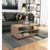 Stolik kawowy na kółkach w kolorze dąb sonoma mat, o wymiarach 90x51x40 cm, stoi na dywanie w salonie, obok ciemnej sofy z poduszkami. Na stoliku znajduje się taca z karafką i szklankami, a w tle widoczny jest regał z książkami oraz lampa stojąca.
