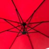 Czerwony parasol ogrodowy z widoczną konstrukcją metalowych żeber rozpościerających się promieniście od centralnego punktu. Materiał parasola jest napięty, tworząc równomierną powierzchnię.