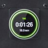 Na zdjęciu widoczny jest wyświetlacz z okrągłą ramką, na którym znajduje się napis "TIME" oraz cyfry "0:01:26" i "16.0 KM/H". Tło jest ciemne, a wyświetlacz otoczony jest zieloną poświatą.