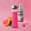 Na zdjęciu znajduje się różowa butelka z metalową nakrętką oraz produkt "OSHEE DROP IN Vitamin Lemonade" o smaku maliny i grejpfruta, obok którego leżą połówka grejpfruta i malina. Na etykiecie widnieje tekst: "NEW koncentrat aż do 10L napoju, HYDROCONCEN