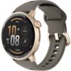 Złoty smartwatch z okrągłym wyświetlaczem, na którym widoczne są informacje: godzina 10:08 AM, data środa 20, poziom naładowania baterii 80%, wysokość 6000 FT oraz liczba kroków 10000. Pasek zegarka jest szary, a na tarczy znajduje się przycisk z czerwonym akcentem.