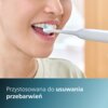 Osoba używa elektrycznej szczoteczki do zębów, a na dole zdjęcia znajduje się tekst: "Przystosowana do usuwania przebarwień".