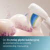 Na zdjęciu widoczna jest szczoteczka do zębów z niebiesko-zielonymi włóknami, czyszcząca powierzchnię zębów z fioletowymi drobinkami. Na dole znajduje się tekst: "Do 7x mniej płytki bakteryjnej w porównaniu ze zwykłą szczoteczką manualną".