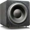 Czarny subwoofer z widocznym logo "SVS" na przednim panelu, umieszczony na drewnianej obudowie o wyraźnej teksturze. Produkt ma okrągły głośnik z metalicznym wykończeniem.