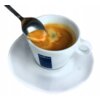 Na zdjęciu widoczna jest filiżanka z espresso na spodku, z łyżeczką unoszącą piankę kawy. Na filiżance znajduje się logo "LAVAZZA".