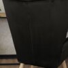 Czarny welurowy fotel z widocznym szwem na tylnej części oparcia, stojący na drewnianych nogach. W tle fragment jasnej ściany z delikatnym wzorem oraz fragment blatu.