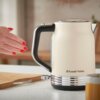 Kremowy czajnik elektryczny z czarną rączką i chromowanymi elementami stoi na blacie kuchennym. Na czajniku widoczne jest logo "Russell Hobbs".