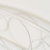 Zdjęcie przedstawia fragment białego, metalowego łóżka z ozdobnym, zaokrąglonym wzorem na wezgłowiu. Konstrukcja jest wykonana z cienkich, metalowych prętów, które tworzą symetryczne, okrągłe kształty.