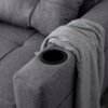 Szara, rozkładana sofa z widocznym podłokietnikiem, w którym znajduje się uchwyt na napoje. Na podłokietniku leży złożony, jasnoszary koc.