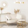 Kremowa sofa dwuosobowa o eleganckim designie stoi na dywanie w jasnym wnętrzu, obok niej znajdują się dwa okrągłe stoliki z marmurowymi blatami i złotymi nogami. W tle widać dekoracyjne lustro, wazon z suszonymi trawami oraz konsolę z książkami i świecam