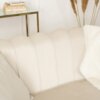 Kremowa sofa dwuosobowa o eleganckim, pikowanym oparciu, z widoczną poduszką w podobnym odcieniu. W tle znajduje się szklany stolik z książkami oraz dekoracyjne trawy w wazonie.