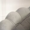 Zbliżenie na oparcie szarej, dwuosobowej sofy z welurowym wykończeniem i ozdobnymi przeszyciami. Tkanina ma delikatny połysk, a struktura materiału jest miękka i gładka.