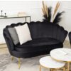 Czarna, dwuosobowa sofa w stylu glamour z zaokrąglonym oparciem, ozdobiona dwoma poduszkami w odcieniach szarości i bieli, stoi na złotych nóżkach. W tle widoczny jest stolik z książkami i dekoracyjne trawy, a na pierwszym planie okrągłe stoliki z marmuro