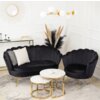 Czarna sofa dwuosobowa i fotel wypoczynkowy w stylu glamour z zaokrąglonymi oparciami, ustawione na jasnym dywanie, przed trzema okrągłymi stolikami z marmurowymi blatami i złotymi nogami. W tle widoczna jest dekoracja ścienna w formie okrągłego lustra, s