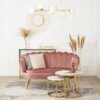 Na zdjęciu znajduje się różowa sofa dwuosobowa w stylu glamour z ozdobnymi poduszkami, ustawiona na jasnym dywanie z wzorem. Przed sofą stoją dwa okrągłe stoliki z marmurowymi blatami i złotymi nogami, a w tle widać dekoracyjne lustro, lampę sufitową oraz