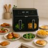 Na zdjęciu znajduje się czarna frytkownica beztłuszczowa z podwójnym koszem, na której wyświetlaczu widnieje temperatura "180°C 180°C", a poniżej znajduje się logo "alpina". Wokół frytkownicy rozmieszczone są talerze z różnymi potrawami, takimi jak brokuł