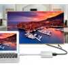 Na zdjęciu widać laptopa oraz telewizor, na których wyświetlany jest ten sam obraz przedstawiający marinę z jachtami o zachodzie słońca. Laptop jest połączony z telewizorem za pomocą srebrnego adaptera USB Typu C.