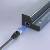 Szara stacja dokująca z widocznym portem Ethernet, do którego zbliża się czarny kabel sieciowy z niebieskimi efektami świetlnymi. Na obudowie stacji widoczny jest fragment napisu "zen".