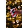 Osoba trzyma opakowanie napoju "BARÚ Swirly Hot Chocolate Powder 250 g" na tle rozświetlonej choinki. Na opakowaniu widnieje napis: "Naturally Good Treats" oraz "Genuine Chocolate".
