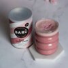 Puszka z napisem "BARÚ Pink Chai Latte with black tea, beetroot & exotic spices" stoi obok szklanki z różowym napojem, na której powierzchni znajdują się małe, różowe kuleczki. Na puszce widnieje również napis "Vegan Recipe" oraz "Surreally Good Treats".