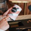 Na zdjęciu widoczna jest puszka z napisem "BARÚ Surreally Good Treats Pink Chai Latte with black tea, beetroot & exotic spices" trzymana w dłoni. Puszka ma różowo-białe paski, a na górze widnieje napis "VEGAN RECIPE".