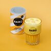 Puszka z napisem "BARÚ Surreally Good Treats Golden Chai Latte with turmeric, black tea & exotic spices" stoi obok szklanki z żółtym napojem. Na szklance widnieje logo "BARÚ".