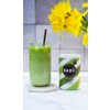 Na zdjęciu znajduje się szklanka z zielonym napojem z lodem i słomką, obok której stoi puszka z napisem "BARÚ Matcha Latte with green tea". W tle widoczne są żółte kwiaty oraz jasna, kafelkowa ściana.