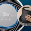 Na zdjęciu widoczny jest panel oczyszczacza powietrza z wyświetlaczem pokazującym wartość "008" oraz ikonami, a obok znajduje się filtr z napisem "Philips FY2200". Filtr jest trzymany przez rękę, a tło stanowi powierzchnia drewniana.