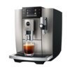 Srebrny ekspres do kawy z wyświetlaczem pokazującym opcje napojów, takich jak Espresso, Coffee, Americano i Cappuccino, z logo "jura" oraz "E8" na przednim panelu. Pod dyszami znajduje się szklanka z kawą.