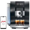 Czarny ekspres do kawy z wyświetlaczem dotykowym pokazującym opcje: Espresso, Coffee, Lungo, Cappuccino, oraz dwoma filiżankami kawy na tacy. Obok ekspresu widoczny jest smartfon z logo "jura" i napisem "J.O.E.".