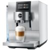 Srebrny ekspres do kawy z wyświetlaczem dotykowym, na którym widoczne są opcje: Espresso, Coffee, Lungo, Cappuccino. Na tacy ociekowej stoi szklanka z warstwową kawą z mleczną pianką, a na froncie ekspresu znajduje się logo "jura Z10".